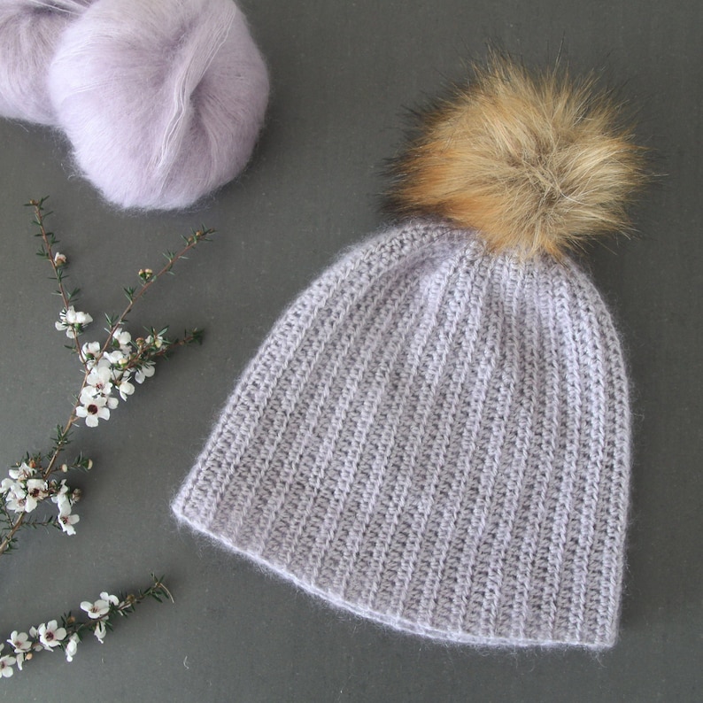 May include: A light purple knitted beanie with a brown faux fur pom pom.