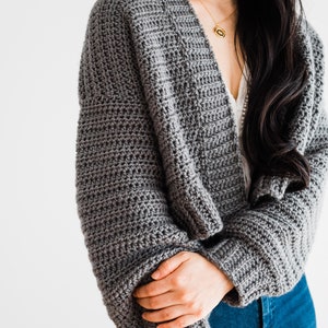 May include: A gray crocheted cardigan with long sleeves and a V-neck. The cardigan is worn by a person with long black hair.