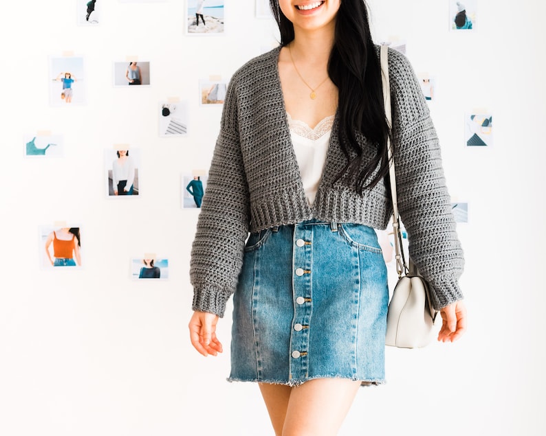 May include: A gray cropped cardigan with long sleeves and a V-neckline. The cardigan is worn over a white camisole and a denim skirt with button closures.