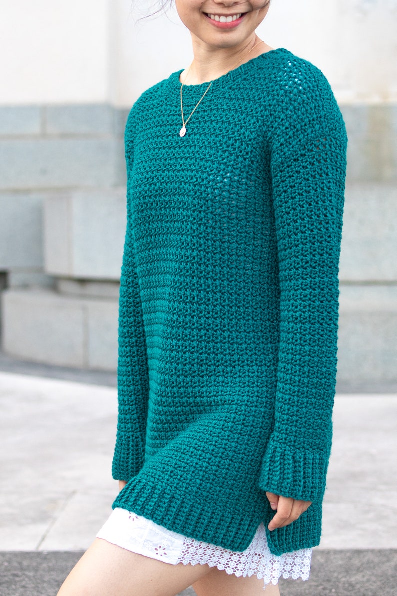 May include: A teal blue crocheted sweater with long sleeves and a loose fit.