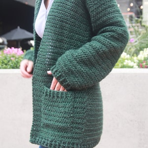 May include: A dark green crocheted cardigan with pockets. The cardigan is open in the front and has long sleeves.