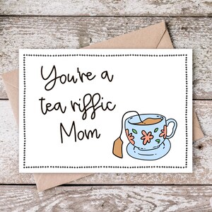 May include: A white card with black text that reads "You're a tea riffic Mom" and a cartoon illustration of a teacup with a tea bag. The card has a black dotted border.
