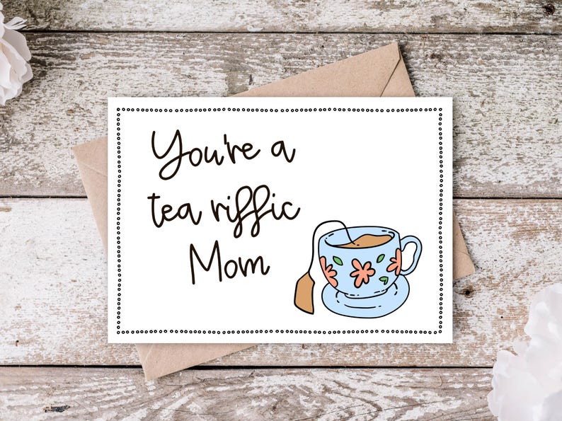 May include: A white card with black text that reads "You're a tea riffic Mom" and a cartoon illustration of a teacup with a tea bag. The card has a black dotted border.