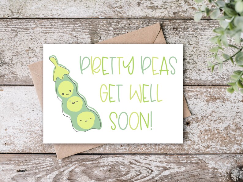May include: A white greeting card with the text "Pretty Peas Get Well Soon!" in green and a cartoon pea pod illustration. The card is on a wooden surface with a brown envelope.