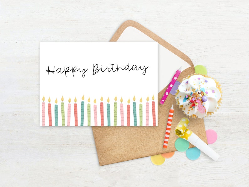 May include: A white birthday card with the words "Happy Birthday" in black script, featuring colorful candles at the bottom. The card is inside a brown envelope, with a cupcake, candles, and confetti.
