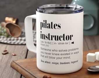 May include: White ceramic travel mug with a black design that reads "pilates instructor" with a definition and the words "ninja, badass, legend".