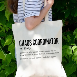 Puede incluir: Una bolsa de tela blanca con texto negro que dice "CHAOS COORDINATOR (n.) Emily Alguien que resuelve problemas que nunca supiste que existían de una manera que te hará volar la mente. Ver también: hacedor de milagros; rockstar; leyenda"
