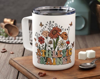 Può includere: Una tazza in ceramica bianca con un motivo floreale e il testo "Rockstar Legend Ninja Athletic Trainer".