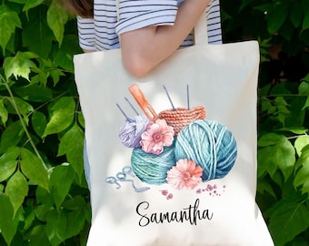 May include: A white canvas tote bag with a colorful illustration of yarn balls, knitting needles, and flowers. The bag has the name "Samantha" printed on the front.