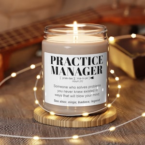 May include: A brown candle with a white label that reads "PRACTICE MANAGER [prak-tes] [ma-ni-jer] noun (n) Someone who solves problems you never knew existed in ways that will blow your mind. See also: ninja: badass: legend"