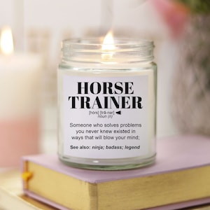 May include: A white candle in a glass jar with a black label that reads "HORSE TRAINER [hórs] [trä-ner] noun (n) Someone who solves problems you never knew existed in ways that will blow your mind; See also: ninja; badass; legend"