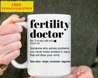 Puede incluir: Taza de cerámica blanca con un diseño negro que dice "fertility doctor" con una definición y las palabras "ninja, rockstar, leyenda".