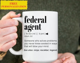 May include: White ceramic mug with a black design that reads "federal agent" and a definition of the word. The definition reads: "['fe-d(ǝ-)rəl] ['ā-jənt] noun (n) Someone who solves problems you never knew existed in ways that will blow your mind. See also: ninja; rocsktar; legend."