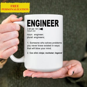 Könnte beinhalten: Eine weiße Keramiktasse mit einem schwarzen Design, auf dem "ENGINEER [en-jǝ-'nir] noun (n) noun: engineer; plural: engineers; 1. Someone who solves problems you never knew existed in ways that will blow your mind. 2. See also ninja; rockstar; legend" steht.