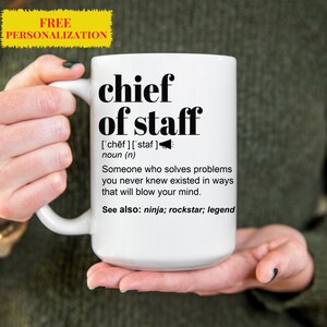 Puede incluir: Taza de cerámica blanca con un diseño negro que dice "jefe de gabinete" y define el término como "Alguien que resuelve problemas que nunca supiste que existían de maneras que te harán volar la mente." La taza también dice "Ver también: ninja; rockstar; leyenda".