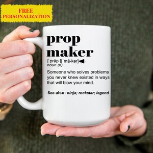 May include: White ceramic mug with the text "prop maker" in a bold, black font. The mug includes a definition of "prop maker" and the words "ninja, rockstar, legend". A yellow banner at the top reads "FREE PERSONALIZATION".
