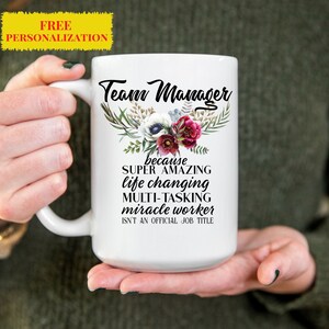 May include: White ceramic coffee mug with a black floral design and the text "Team Manager because SUPER AMAZING life changing MULTI-TASKING miracle worker ISN'T AN OFFICIAL JOB TITLE"