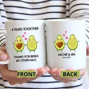 Puede incluir: Dos tazas blancas con una ilustraci&oacute;n de una pareja de aguacates tomados de la mano. El texto en la taza delantera dice "4 Years Together Thanks for being my other half." El texto en la taza trasera dice "Archie & Jen since 2015."