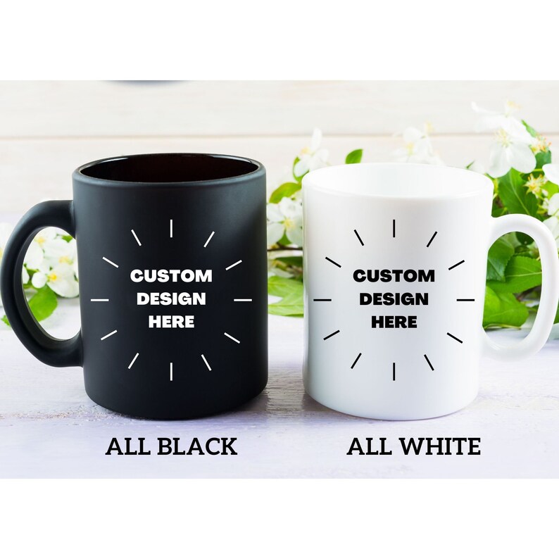 May include: Two ceramic coffee mugs, one black and one white, with a white design that says "CUSTOM DESIGN HERE" in a circle with lines radiating out from the center. The mug on the left is labeled "ALL BLACK" and the mug on the right is labeled "ALL WHITE".