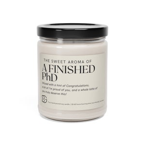 May include: A white soy candle in a glass jar with a black lid. The label reads "The Sweet Aroma of A Finished PhD" and includes the text "Infused with a hint of Congratulations, a bit of I'm proud of you, and a whole lotta of you truly deserve this!"