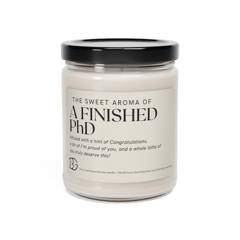 May include: A white soy candle in a glass jar with a black lid. The label reads "The Sweet Aroma of A Finished PhD" and includes the text "Infused with a hint of Congratulations, a bit of I'm proud of you, and a whole lotta of you truly deserve this!"