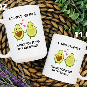 Puede incluir: Dos tazas de cer&aacute;mica blanca con un dise&ntilde;o de dos mitades de aguacate que se toman de la mano. El texto en las tazas dice "4 a&ntilde;os juntos" y "Gracias por ser mi otra mitad.". Las tazas est&aacute;n disponibles en tama&ntilde;os de 11 oz y 15 oz.