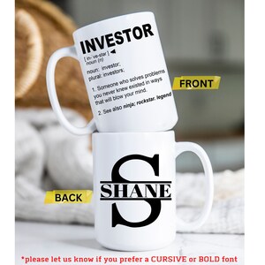 May include: White ceramic mug with a black handle. The front of the mug has the word "INVESTOR" defined as "Someone who solves problems you never knew existed in ways that will blow your mind." The back of the mug has a large black letter "S" with the name "SHANE" written across the middle of the letter.