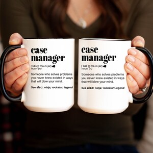 May include: Two white ceramic mugs with black handles and black rims. The mugs feature the text "case manager" with a definition and the words "ninja, rockstar, legend".