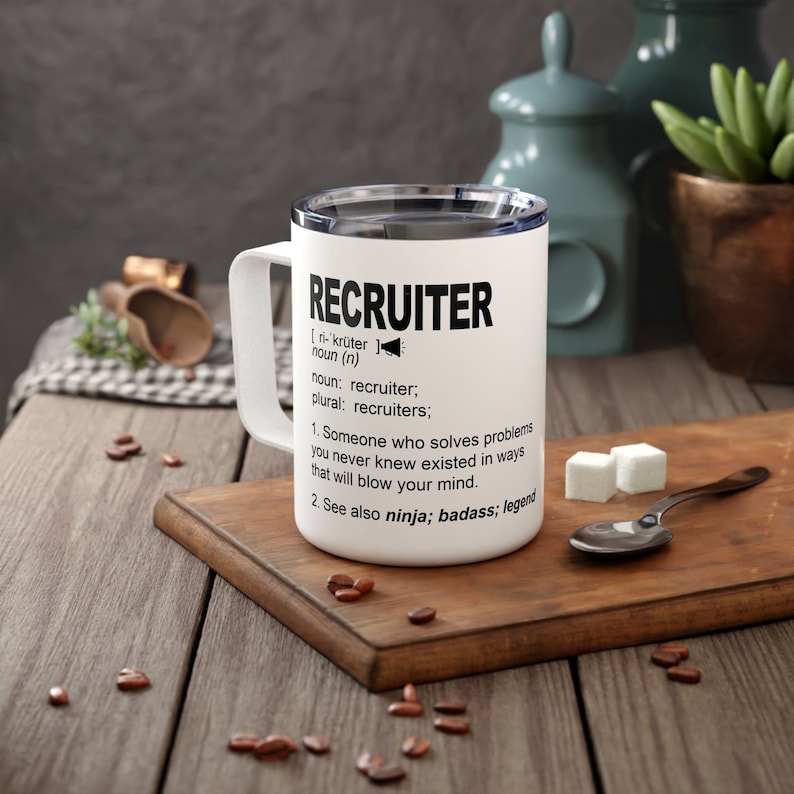 May include: White travel mug with a black definition of the word "Recruiter" printed on it. The definition reads: "Someone who solves problems you never knew existed in ways that will blow your mind. See also ninja; badass; legend."