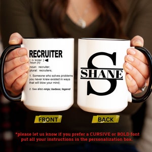 May include: White ceramic coffee mug with a black handle. The front of the mug has the word "RECRUITER" defined as "Someone who solves problems you never knew existed in ways that will blow your mind". The back of the mug has the name "SHANE" written in black letters across a large black letter "S".