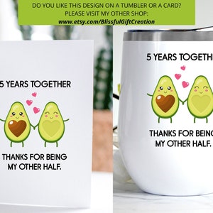 Puede incluir: Una tarjeta blanca y un vaso blanco con un dise&ntilde;o de dos aguacates de dibujos animados tomados de la mano. Los aguacates tienen corazones marrones en su interior y corazones rosas flotando sobre ellos. El texto en ambos art&iacute;culos dice "5 Years Together" y "Thanks for being my other half."