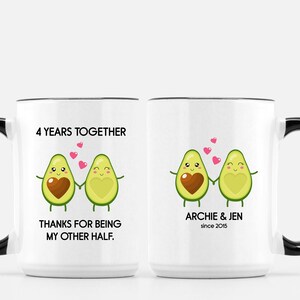 Puede incluir: Dos tazas blancas con asas negras. Una taza tiene el texto "4 Years Together" y "Thanks for being my other half." con una pareja de aguacates de dibujos animados. La otra taza tiene el texto "Archie & Jen since 2015" con una pareja de aguacates de dibujos animados.