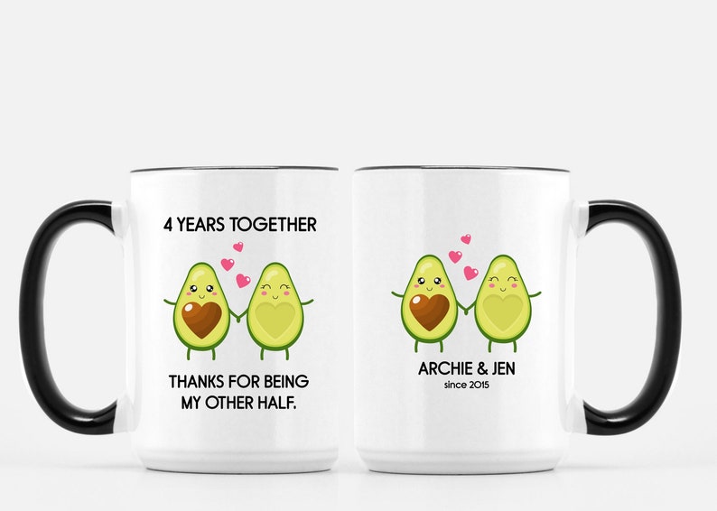 Puede incluir: Dos tazas blancas con asas negras. Una taza tiene el texto "4 Years Together" y "Thanks for being my other half." con una pareja de aguacates de dibujos animados. La otra taza tiene el texto "Archie & Jen since 2015" con una pareja de aguacates de dibujos animados.