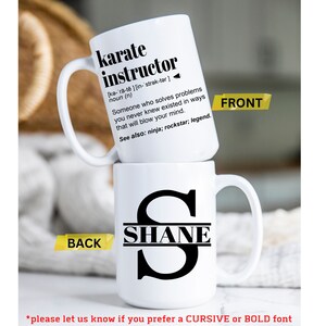 May include: White ceramic mug with a black handle. The front of the mug has the text "karate instructor" with a definition. The back of the mug has a black letter "S" with the name "SHANE" written across the middle of the letter.