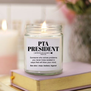 Peut inclure: Une bougie blanche dans un pot en verre avec une étiquette noire qui indique "PTA PRESIDENT" et une définition du mot. L'étiquette comprend également le texte "Voir aussi : ninja ; badass ; légende".