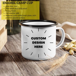 May include: White enamel camp cup with a black rim and handle. The cup features the text "CUSTOM DESIGN HERE" in black. The cup is 12oz and has a glossy finish.