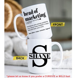 May include: Two white ceramic mugs stacked. The top mug reads "head of marketing" with a definition. The bottom mug features the name "SHANE" in a black font. The front of the top mug is labeled "FRONT" and the back of the bottom mug is labeled "BACK".