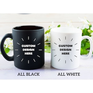 May include: Two ceramic coffee mugs, one black and one white, with the text "CUSTOM DESIGN HERE" in a circle design. The mug on the left is all black and the mug on the right is all white.