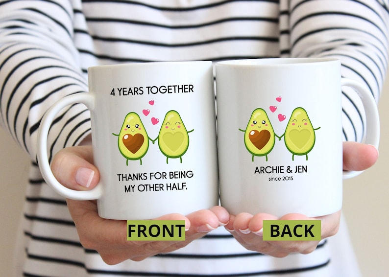Puede incluir: Dos tazas blancas con una ilustraci&oacute;n de una pareja de aguacates tomados de la mano. El texto en la taza delantera dice "4 Years Together Thanks for being my other half." El texto en la taza trasera dice "Archie & Jen since 2015."