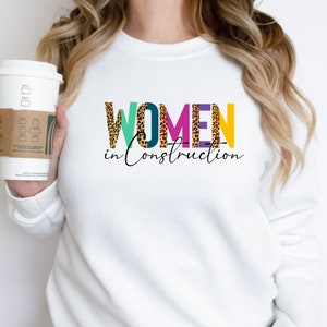 May include: White sweatshirt with the text "WOMEN in Construction" in colorful letters with a leopard print pattern.