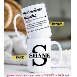 May include: White ceramic mug with a black handle. The front of the mug has a definition for "sport medicine physician" with the text "See also: ninja; rockstar; legend." The back of the mug has a black letter "S" with the name "SHANE" written across the middle.