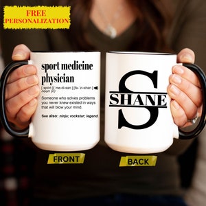 May include: White ceramic mug with a black handle. The front of the mug has a definition for "sport medicine physician" and the back of the mug has a black letter "S" with the name "SHANE" printed above it.