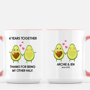Puede incluir: Taza de cer&aacute;mica blanca con borde y asa rosa. La taza presenta un gr&aacute;fico de dos mitades de aguacate que se toman de la mano con corazones en el medio. El texto en la taza dice "4 Years Together" y "Thanks for being my other half." El otro lado de la taza tiene el texto "Archie & Jen since 2015".
