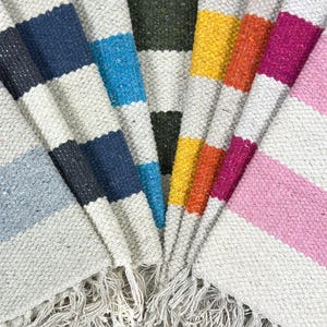 May include: A set of six striped rugs with fringed edges. The rugs are in various colours, including blue, green, yellow, orange, pink, and grey.