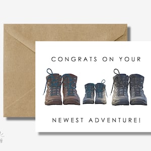 May include: A white card with the text "Congrats on your newest adventure!" and a drawing of four pairs of hiking boots. The boots are brown, gray, and blue.