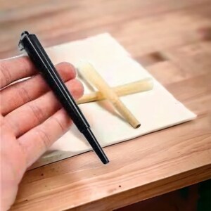 Puede incluir: Una herramienta de rodadura de metal negro con un papel de rodadura de madera sobre una superficie blanca.