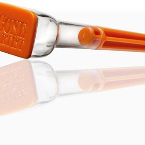 Puede incluir: Herramienta de llenado de cono de plástico naranja con un tubo de plástico transparente y una tapa naranja rectangular que dice "CONE ALCHEMY".