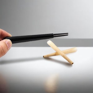 Puede incluir: Una herramienta de enrollado negra con un cono de papel blanco. La herramienta de enrollado se sostiene en una mano y el cono est&aacute; sobre una superficie blanca.