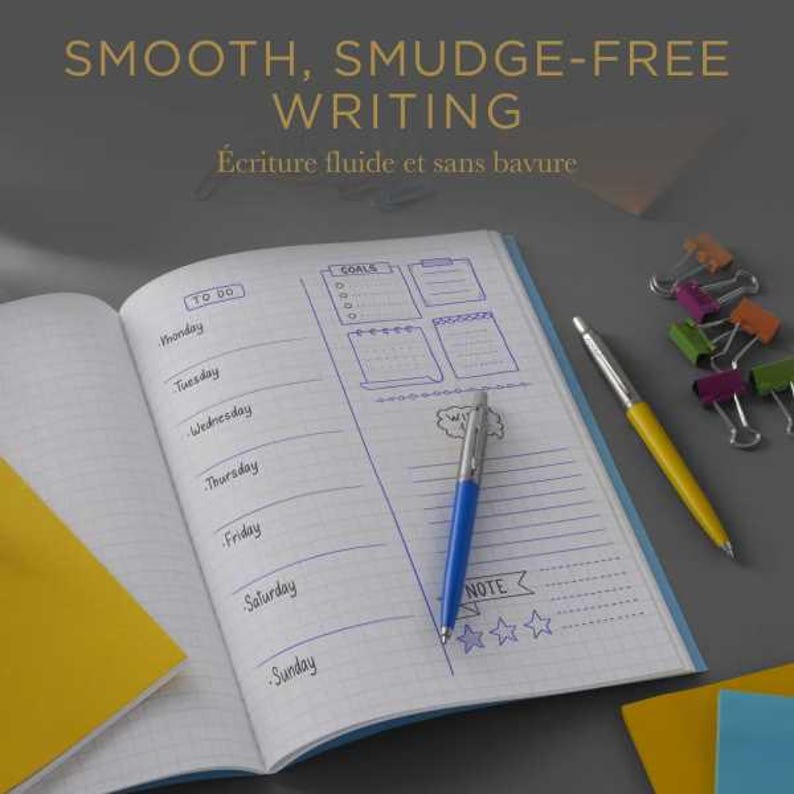 May include: An open planner with grid paper featuring a weekly schedule, a goals section, and a note area with star icons. A blue and silver pen rests on the page. Text reads SMOOTH, SMUDGE-FREE WRITING and &Eacute;criture fluide et sans bavure.