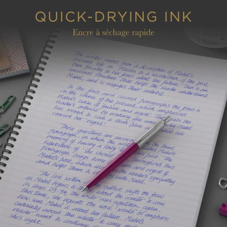 May include: A magenta ballpoint pen with a silver clip and tip rests on a spiral-bound notebook featuring blue ink handwriting. The text "QUICK-DRYING INK" is visible at the top of the image, along with several small green paper clips.
